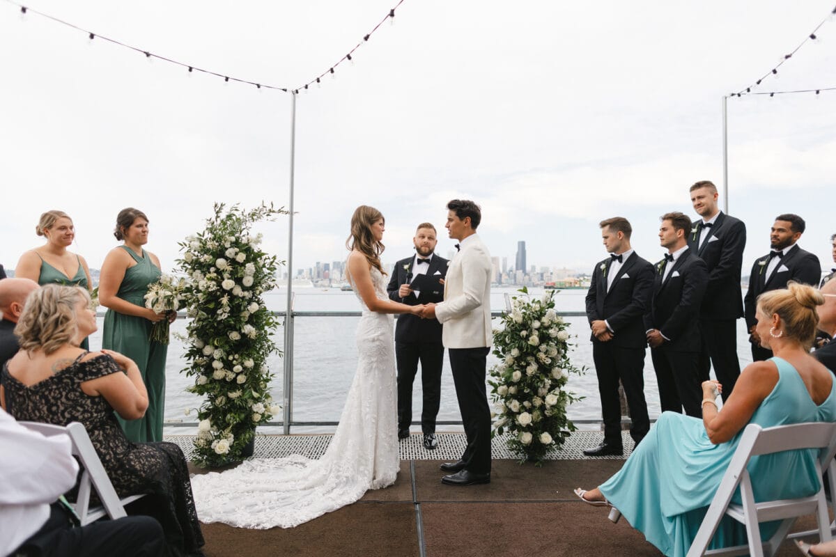 A wedding couple in front of the alter during their ceremony, over looking the Puget Sound and Seattle Skyline from Salty's at Alki.