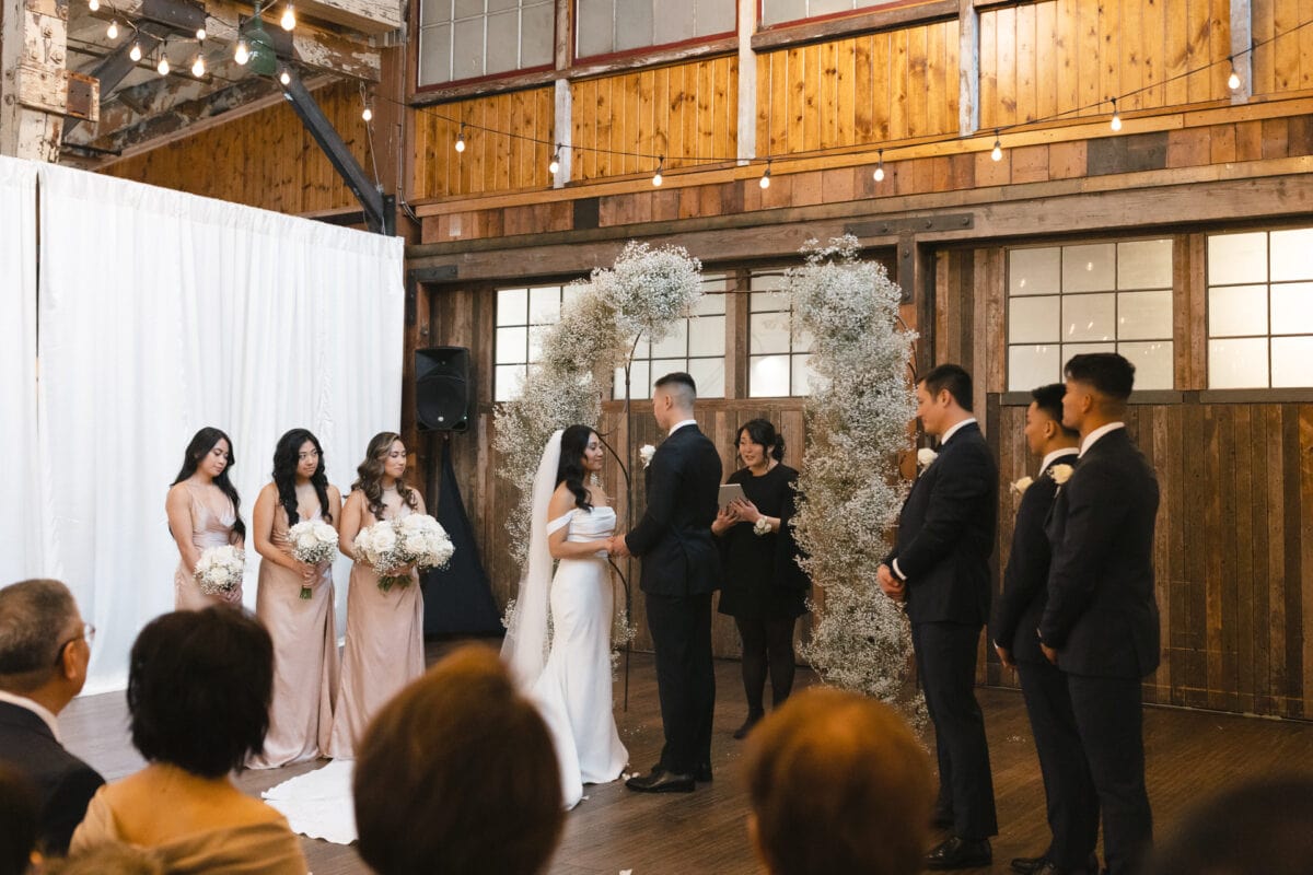 A bride and groom at the front of the alter with their bridal party during the ceremony of their Sodo Park Seattle wedding.